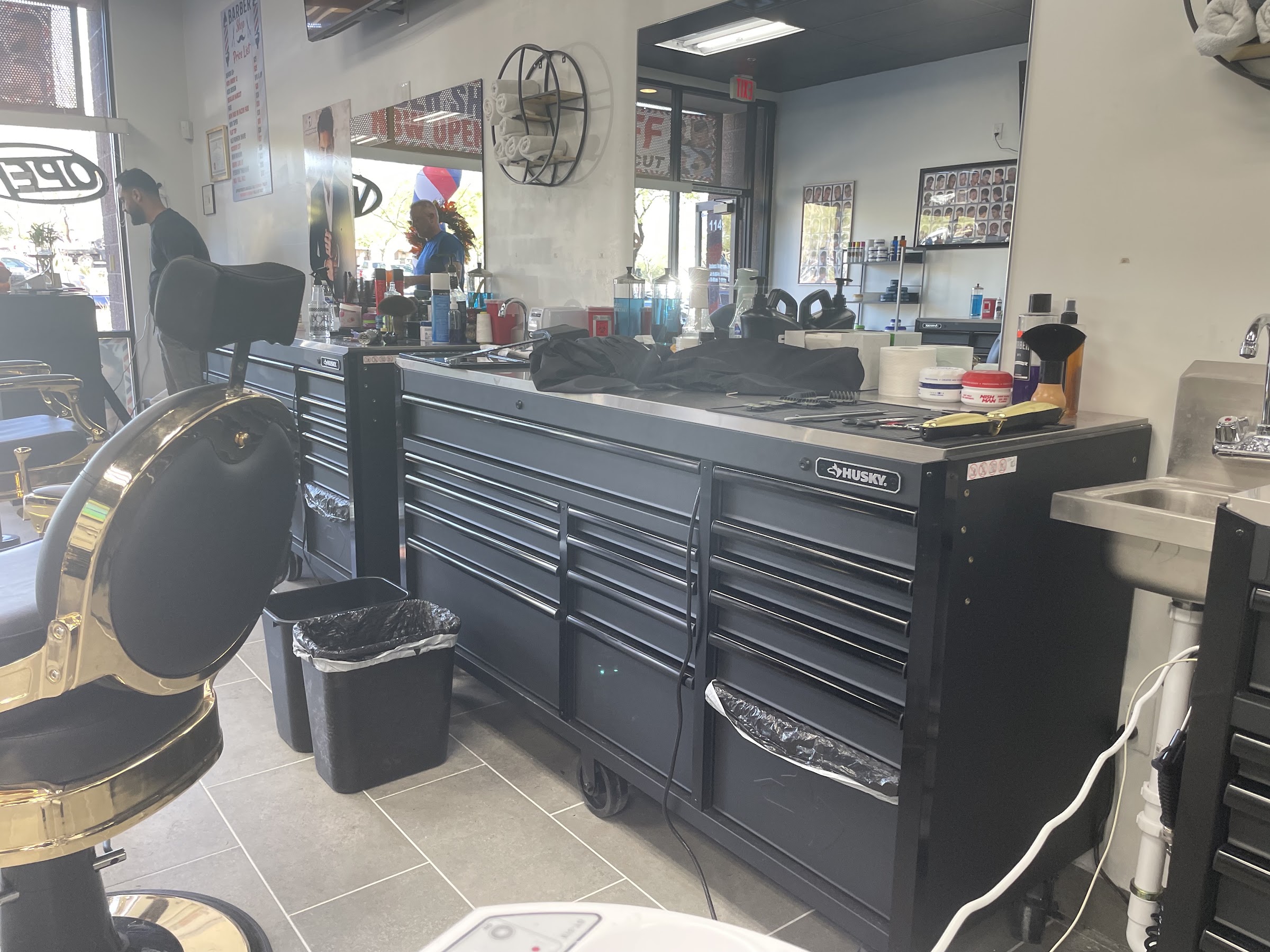 A Kingsman barber station: matte black tool chests, gold clippers and hot towel warmers
