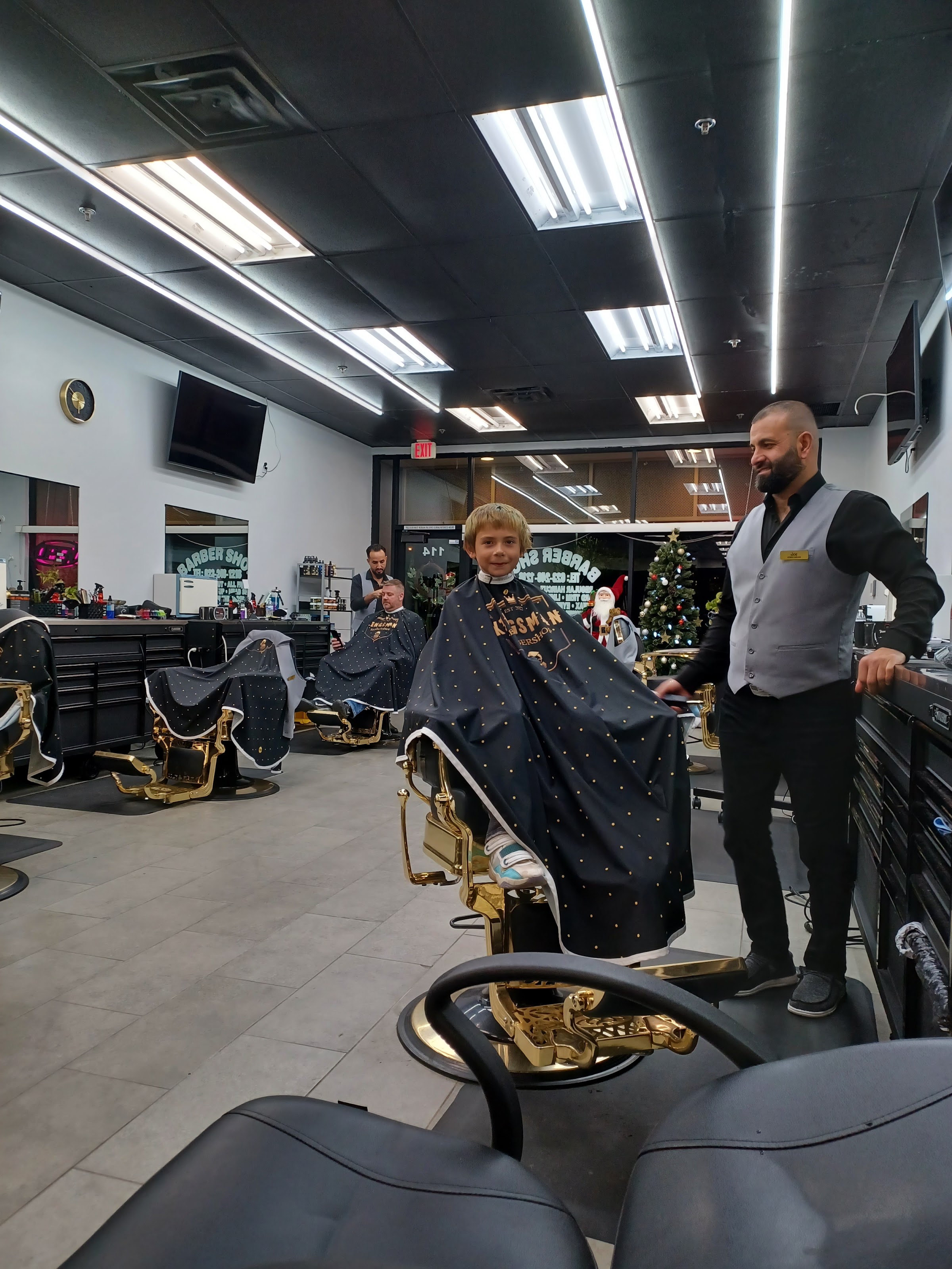 A young client in the chair with his Kingsman barber in uniform vest