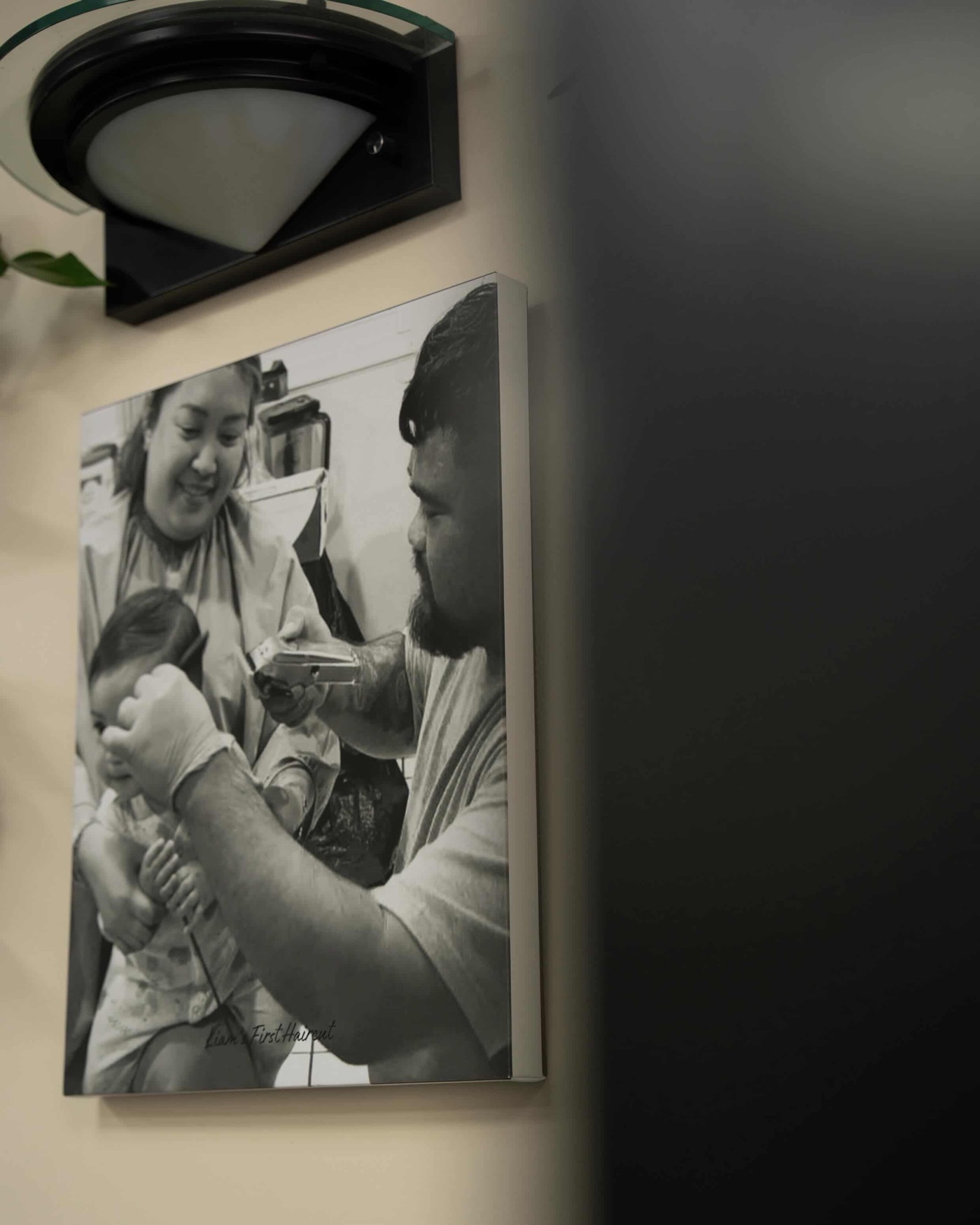 Framed black and white photo of a first haircut at home, hanging on the shop wall